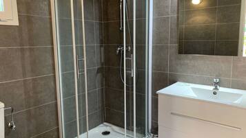 A modern bathroom with a glass-enclosed shower, a white sink, and a large mirror.