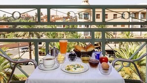 Una mesa en el balcón con alimentos para el desayuno, vistas de edificios y una palmera.