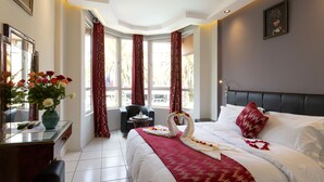 Una habitación de hotel con cama, escritorio con un florero, una silla y ventana con cortinas.