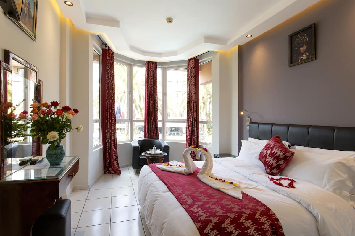 A hotel room with a bed, a desk with a vase of flowers, a chair, and a window with curtains.