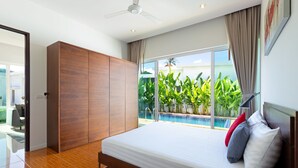 A modern bedroom with a large bed, wooden wardrobe, and a view of a swimming pool. - Tropical Stay at 2BR Pool Villa Greens 8 (Rawai)