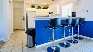 Una cocina con armarios blancos, una pared de acento azul y tres taburetes negros.