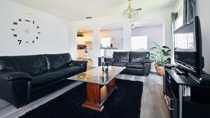 Una sala de estar moderna con un sofá de cuero negro, una mesa de centro de vidrio, un televisor y un reloj en la pared.