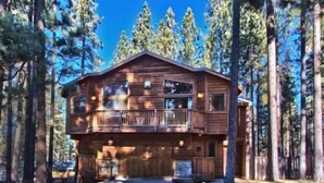A two-story log cabin with a balcony, surrounded by tall pine trees. - Beautiful 6 Bedroom, 4 Bathroom Home Centrally Located and Perfectly Appointed (South Lake Tahoe)