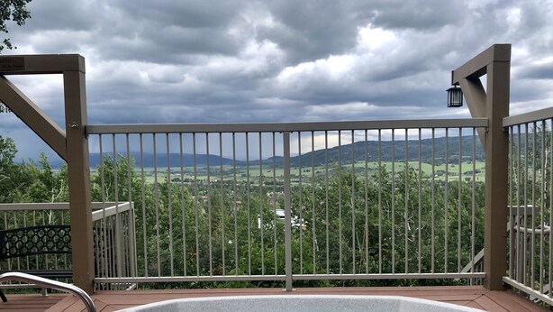 Ein Whirlpool auf einer Terrasse mit Metallgeländer, mit Blick auf eine malerische Landschaft mit Bergen und viel Grün.