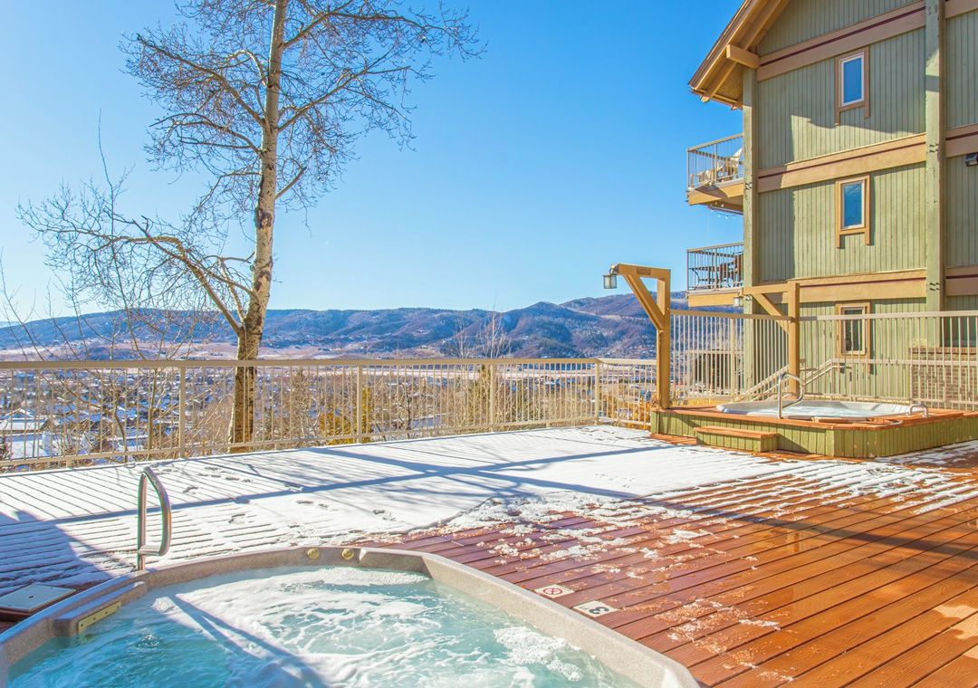 A wooden deck with a hot tub, a wooden building with balconies, and a view of mountains.