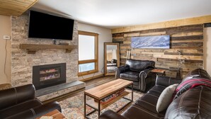 Ein gemütliches Wohnzimmer mit Kamin, Ledersofas, einem Couchtisch und einem Wand-Fernseher.