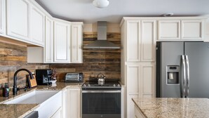 Eine moderne Küche mit weißen Schränken, einem Edelstahl-Kühlschrank, einem eingebauten Backofen und einer Wand mit Holzverkleidung.