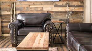 Ein gemütliches Wohnzimmer mit einer Holzwand, einem schwarzen Ledersofa, einem Couchtisch aus Holz mit Büchern und einem gemusterten Teppich.