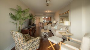 A living room with a sofa, armchair, and ottoman, a TV, a coffee table, and a potted plant.