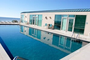 Una piscina con vistas despejadas al océano, un edificio con amplios ventanales y algunas tumbonas.