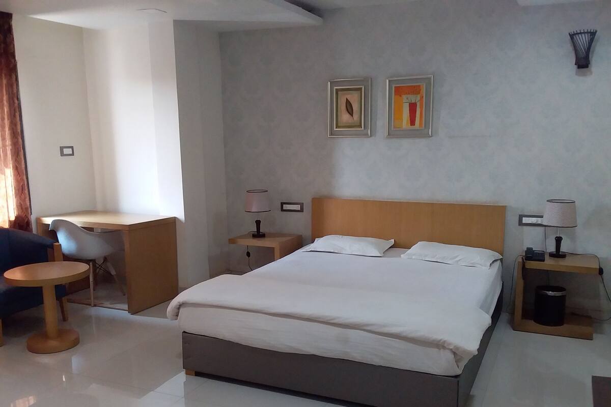 Una habitación de hotel con cama, mesitas de noche, un escritorio y una silla.