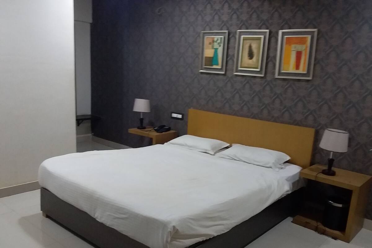 Una cama bien tendida en una habitación de hotel con papel tapiz oscuro estampado, un cabecero de madera y tres cuadros enmarcados en la pared.
