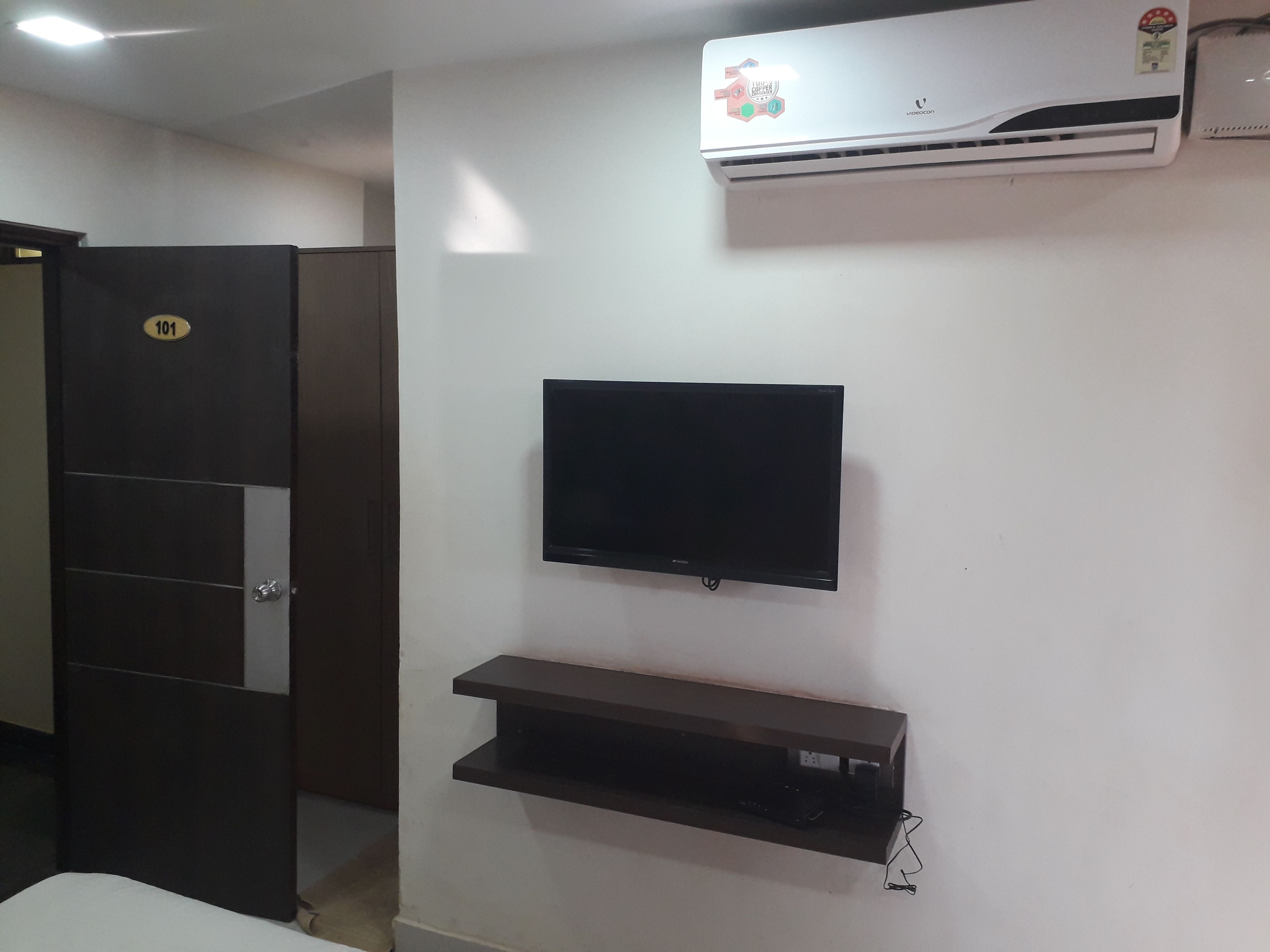 Een kamer met een aan de muur bevestigde televisie, een plank eronder en een airconditioner erboven.