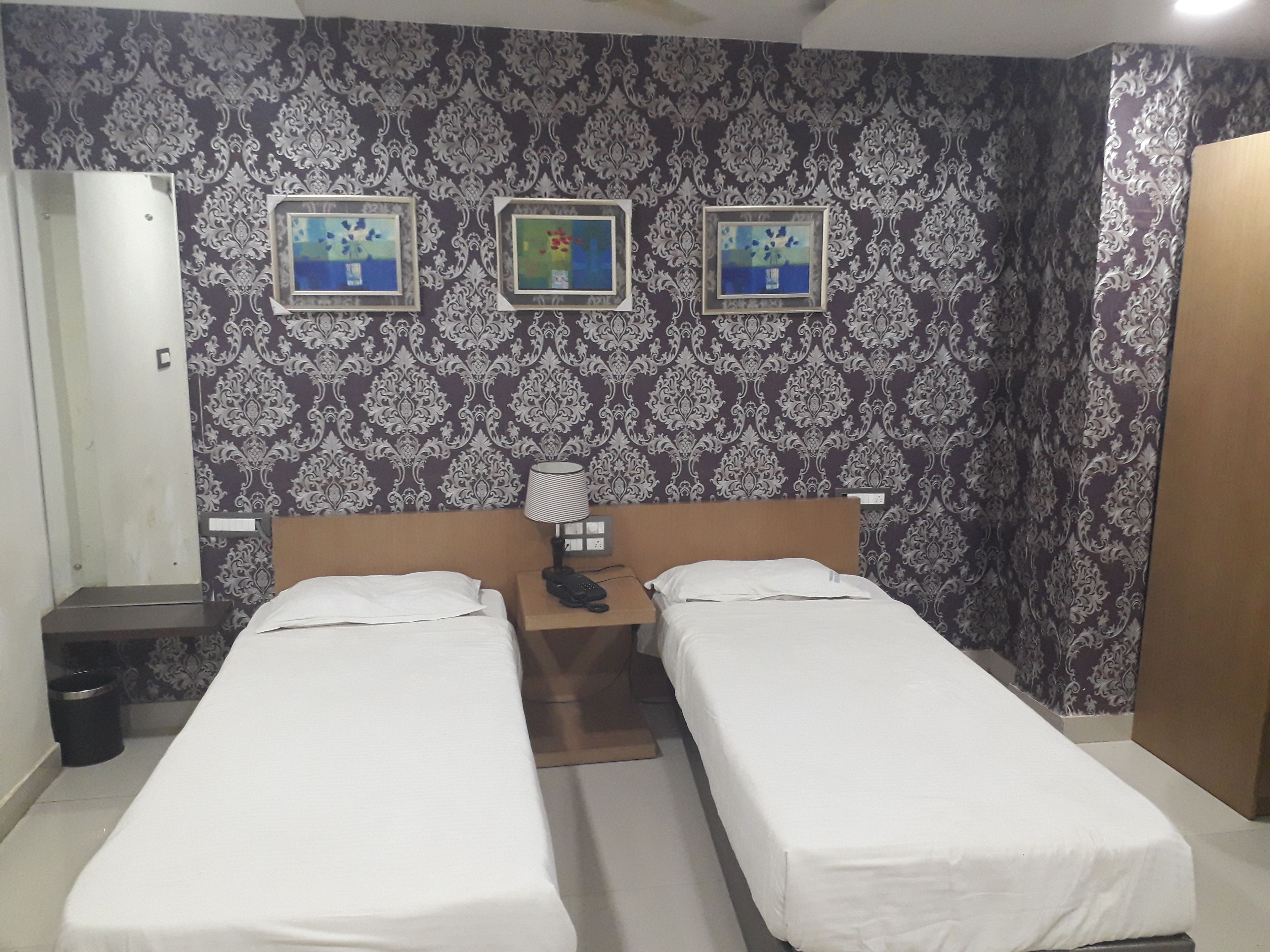 Una habitación de hotel con dos camas individuales, una mesita de noche con lámpara y tres cuadros enmarcados en la pared.