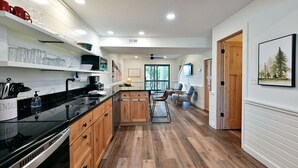 Una cocina moderna con armarios de madera, encimera negra y zona de comedor con mesa y sillas de madera.