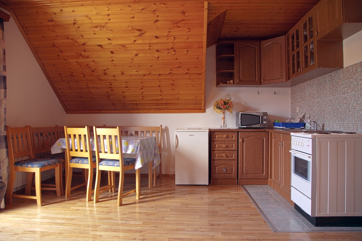 A kitchen with wooden cabinets, a refrigerator, a microwave, and a dining area with chairs and a table.