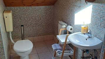 A compact bathroom with a wooden ceiling, a toilet, a sink, and a shower area.