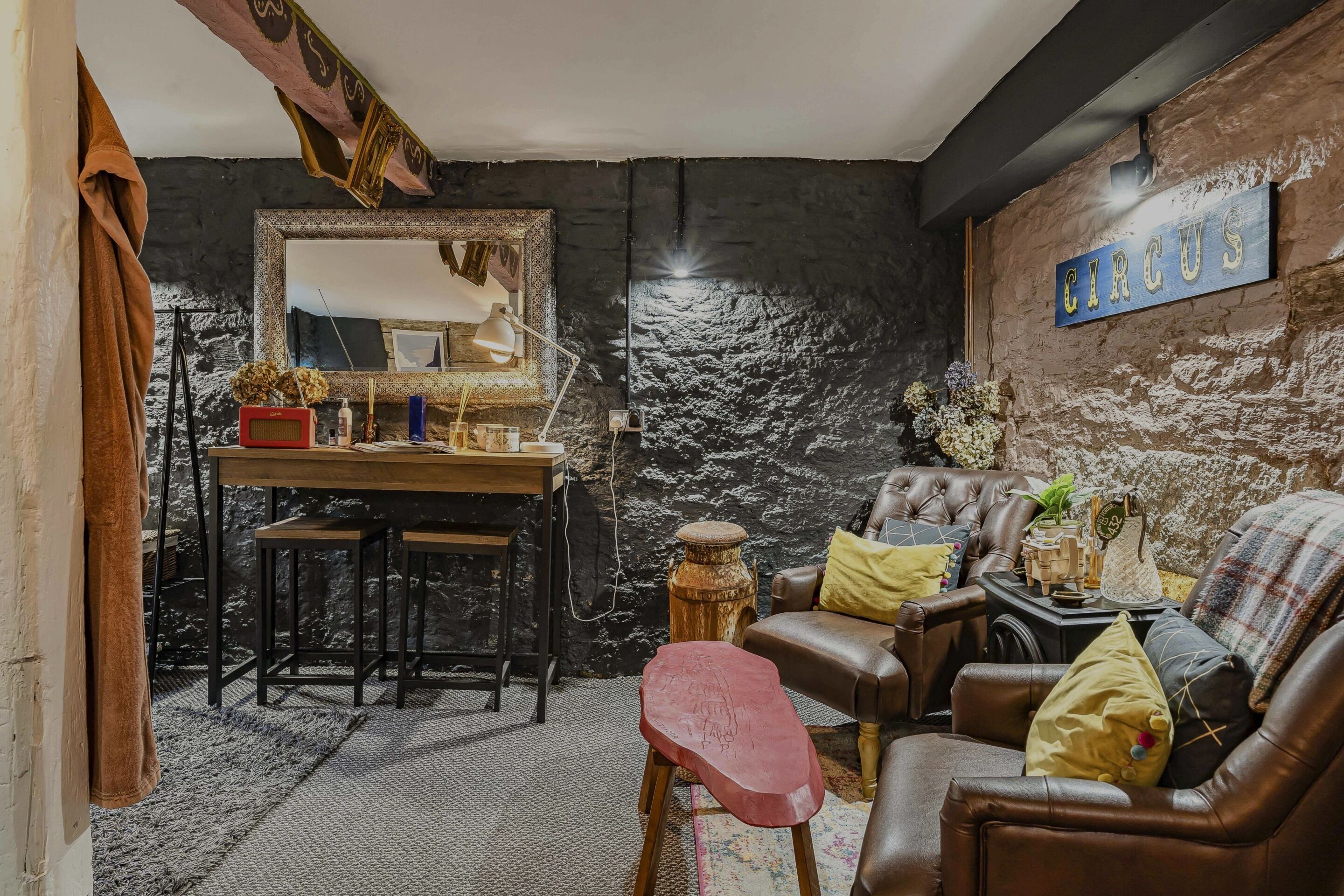 Una habitación con pared de textura oscura, un espejo, un escritorio con lámpara, un sof á de cuero y un letrero que dice 'CIRCUS'.