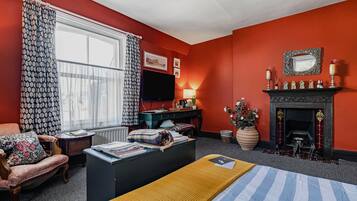 A room with a bed, a desk, a chair, a fireplace, and a television.