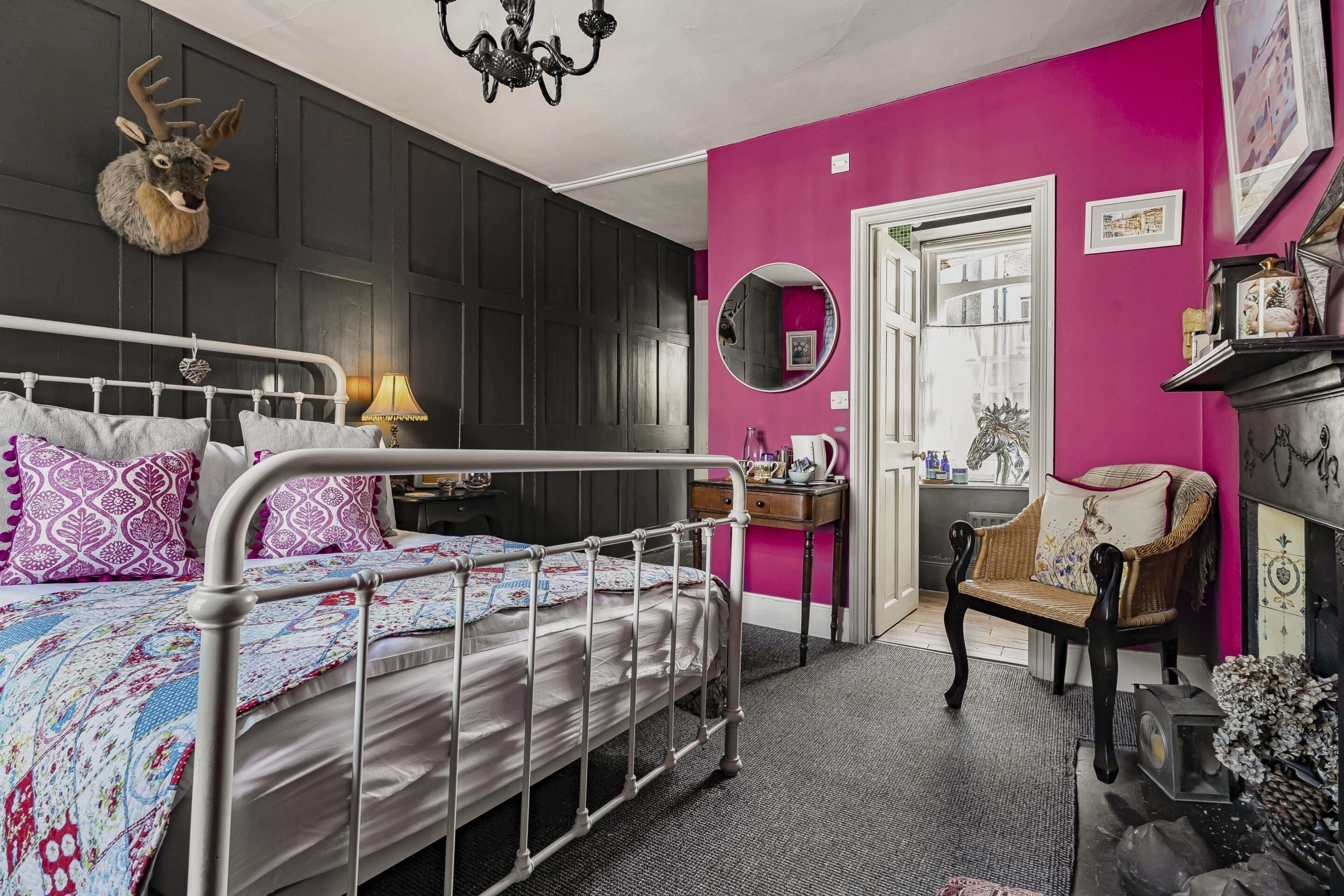 A bedroom with a metal bed frame, a dresser, a chair, a mirror, and a deer head decoration.
