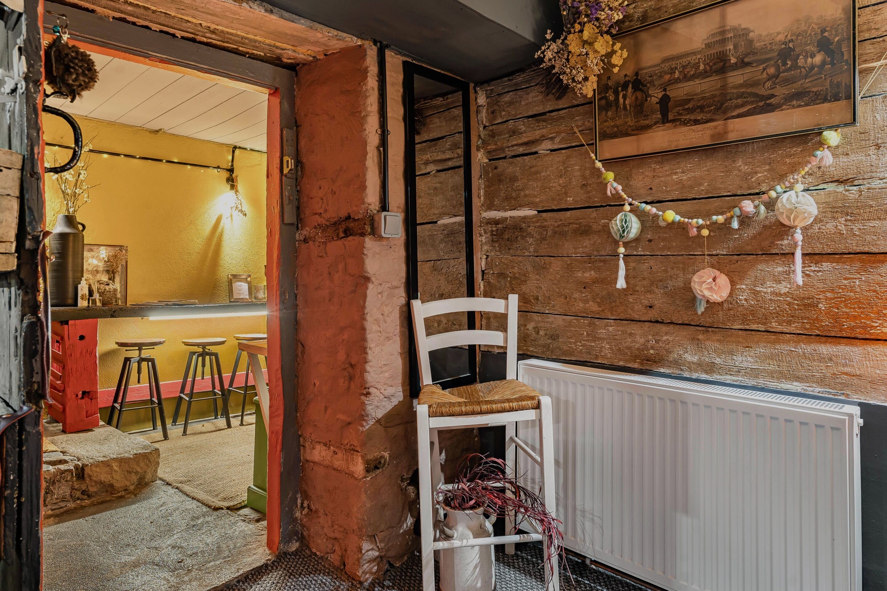 A rustic interior with a white chair, wooden walls, a radiator, and a doorway leading to a bar area.