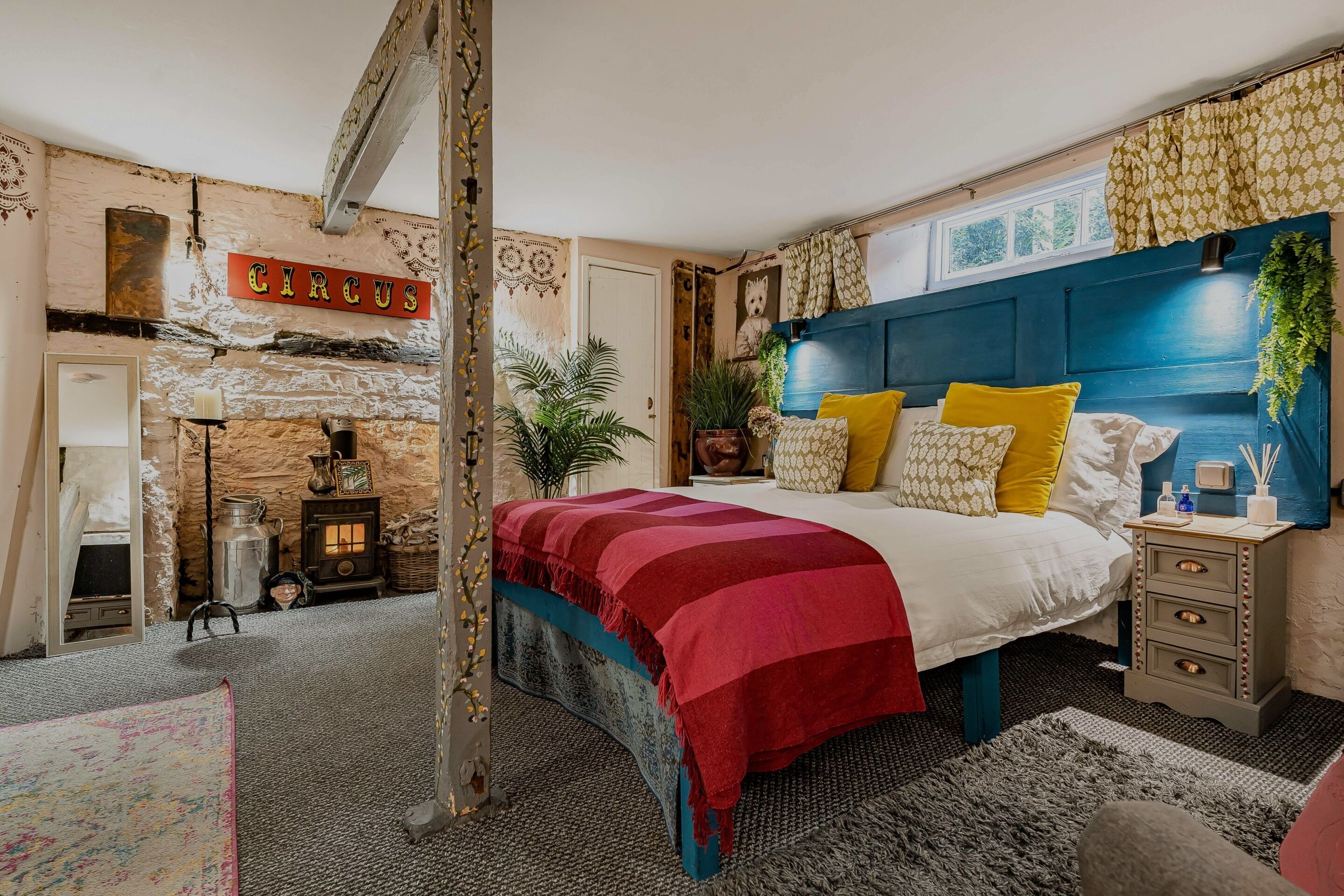 A bedroom with a bed, a nightstand, a wall-mounted headboard, a fireplace, and a sign that reads 'CIRCUS'.