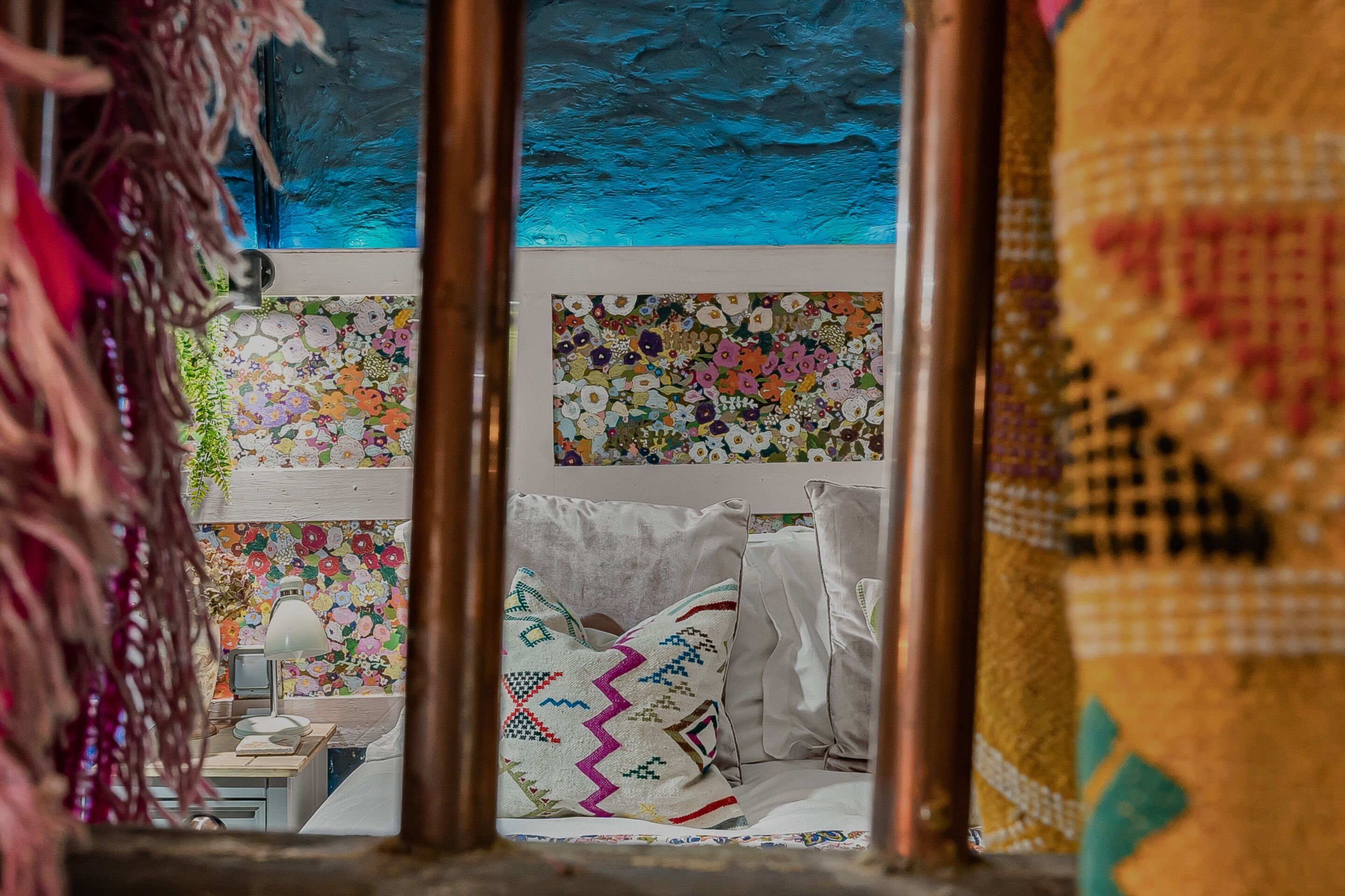 Una habitación con cama, almohadas, mesita de noche y un ventanal con arte floral y abstracto.