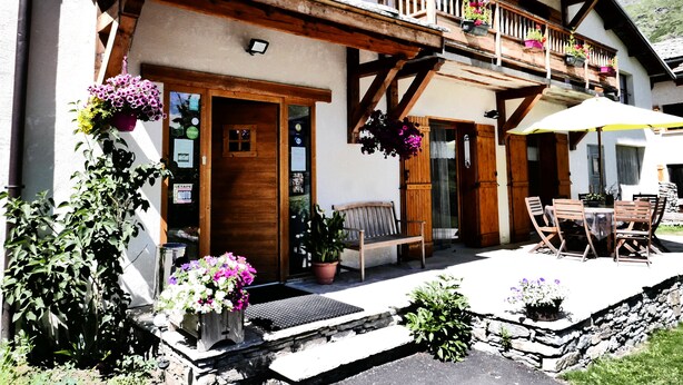 Una cabaña tradicional con balcones de madera, un patio con mobiliario exterior y un paisaje montañoso de fondo.