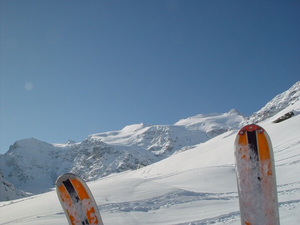 Un par de esquíes sobre una pendiente nevada de montaña bajo un cielo azul despejado.