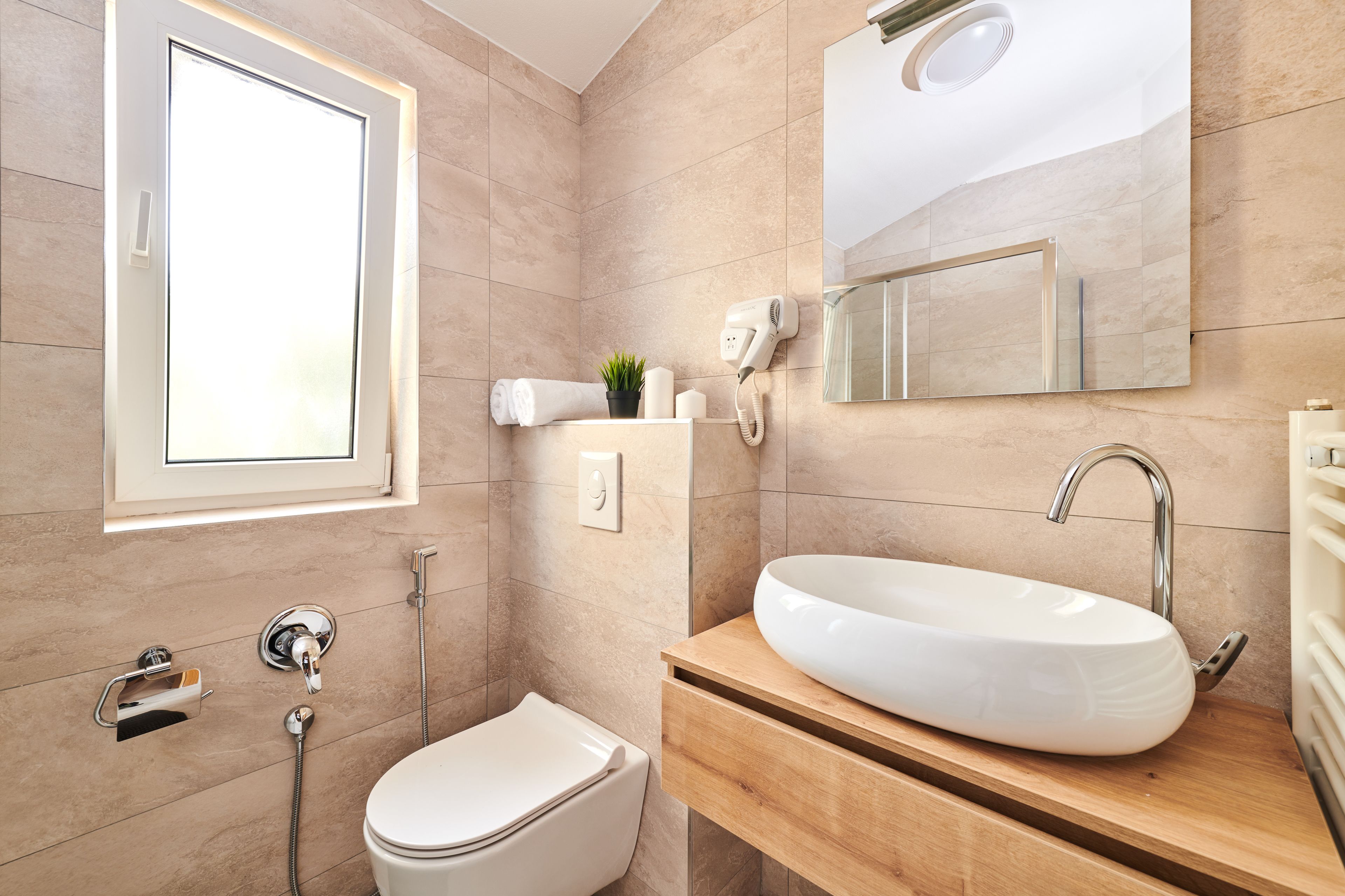 A modern bathroom with a large window, a white sink, a toilet, and a shower.