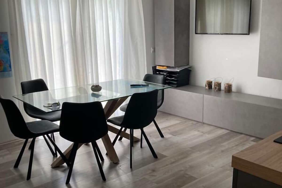 A modern dining area with a glass table, black chairs, and a wooden floor.