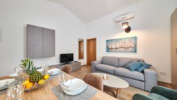 Un salon moderne avec un canapé gris, une table à manger dressée avec des assiettes et des verres, et un tableau représentant des voiliers accroché au mur.