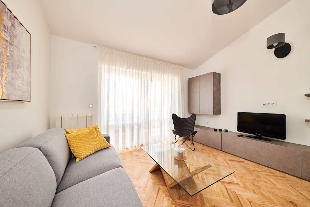 A modern living room with a glass coffee table, grey sofa, and a black chair.