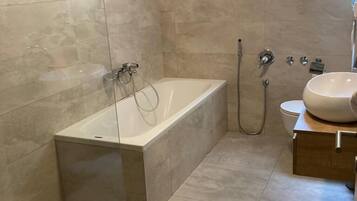 Een moderne badkamer met een vrijstaand bad, toilet en wastafel.
