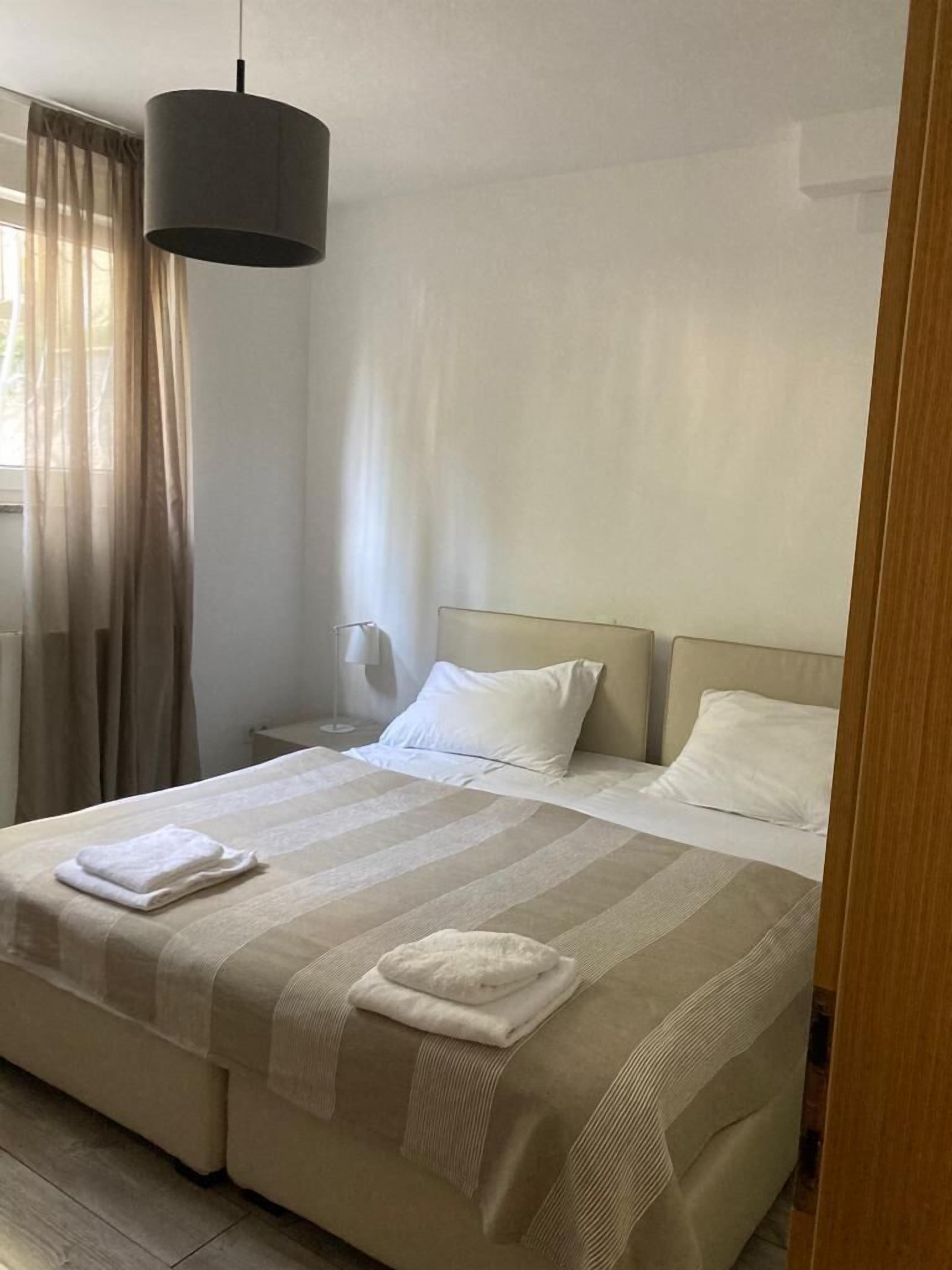 Una habitación de hotel con una cama grande, una mesita de noche, una lámpara y una ventana con cortinas.
