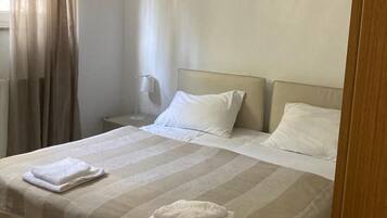 A hotel room with a large bed, a bedside table, a lamp, and a window with curtains.