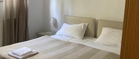 Une chambre d’hôtel avec un grand lit, une table de chevet, une lampe et une fenêtre avec des rideaux.