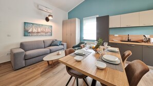 A modern living room with a dining area, a grey sofa, wooden flooring, and a painting of sailboats. - Villa Marija (Pula)