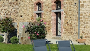 Two lounge chairs in front of a stone building with a brick archway and windows. - La Sellerie (Romagné)