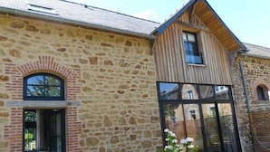 A stone building with a wooden extension, large windows, and a small garden area. - La Sellerie (Romagné)