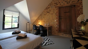 A bedroom with two beds, a desk, and a stone wall. - La Sellerie (Romagné)