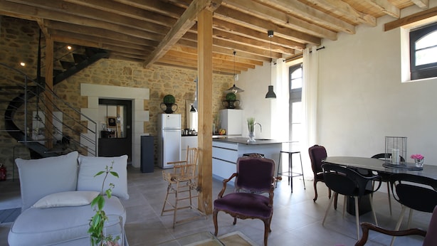 A spacious living area with a sofa, a dining table, and a kitchen in the background. - La Sellerie (Romagné)