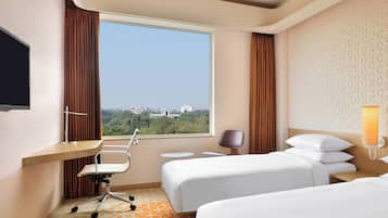 A hotel room with a large window, a desk, two beds, a chair, and a lamp.
