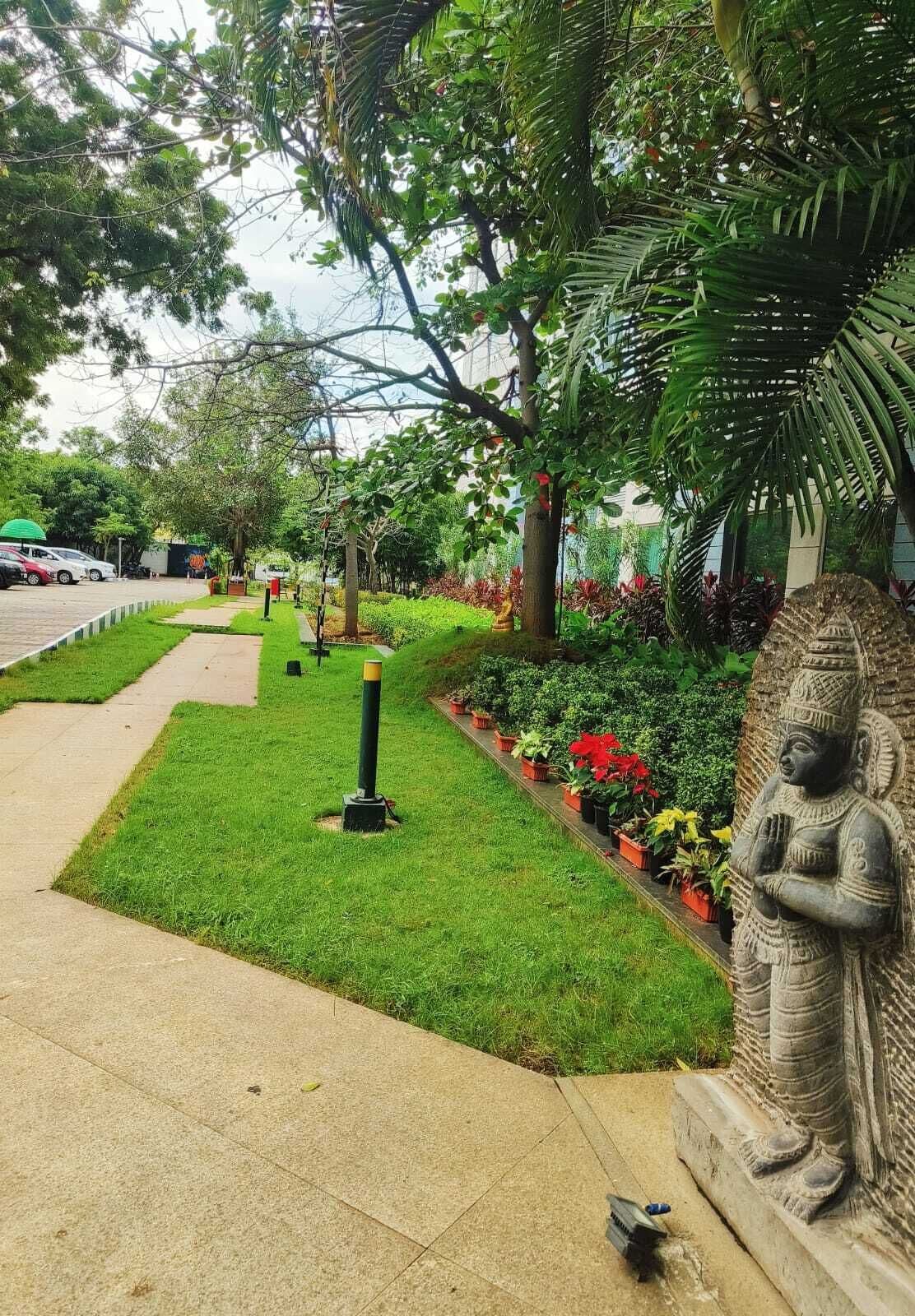 Ein Gartenweg mit einer Statue, Blumentöpfen und einem geparkten Auto im Hintergrund.