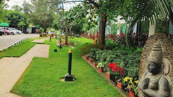 Un sendero en un jardín con una estatua, plantas en macetas y un coche estacionado al fondo.