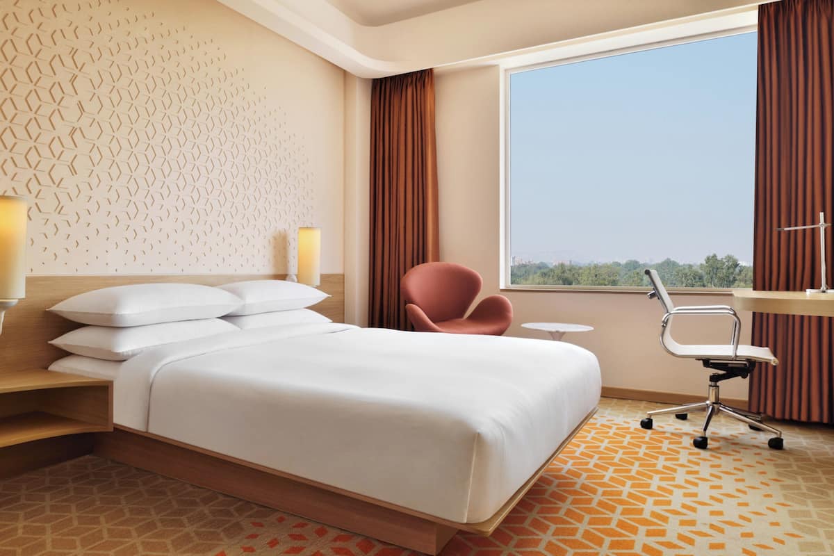 Une chambre d’hôtel avec un grand lit, un bureau, une chaise et une fenêtre donnant sur la ville.