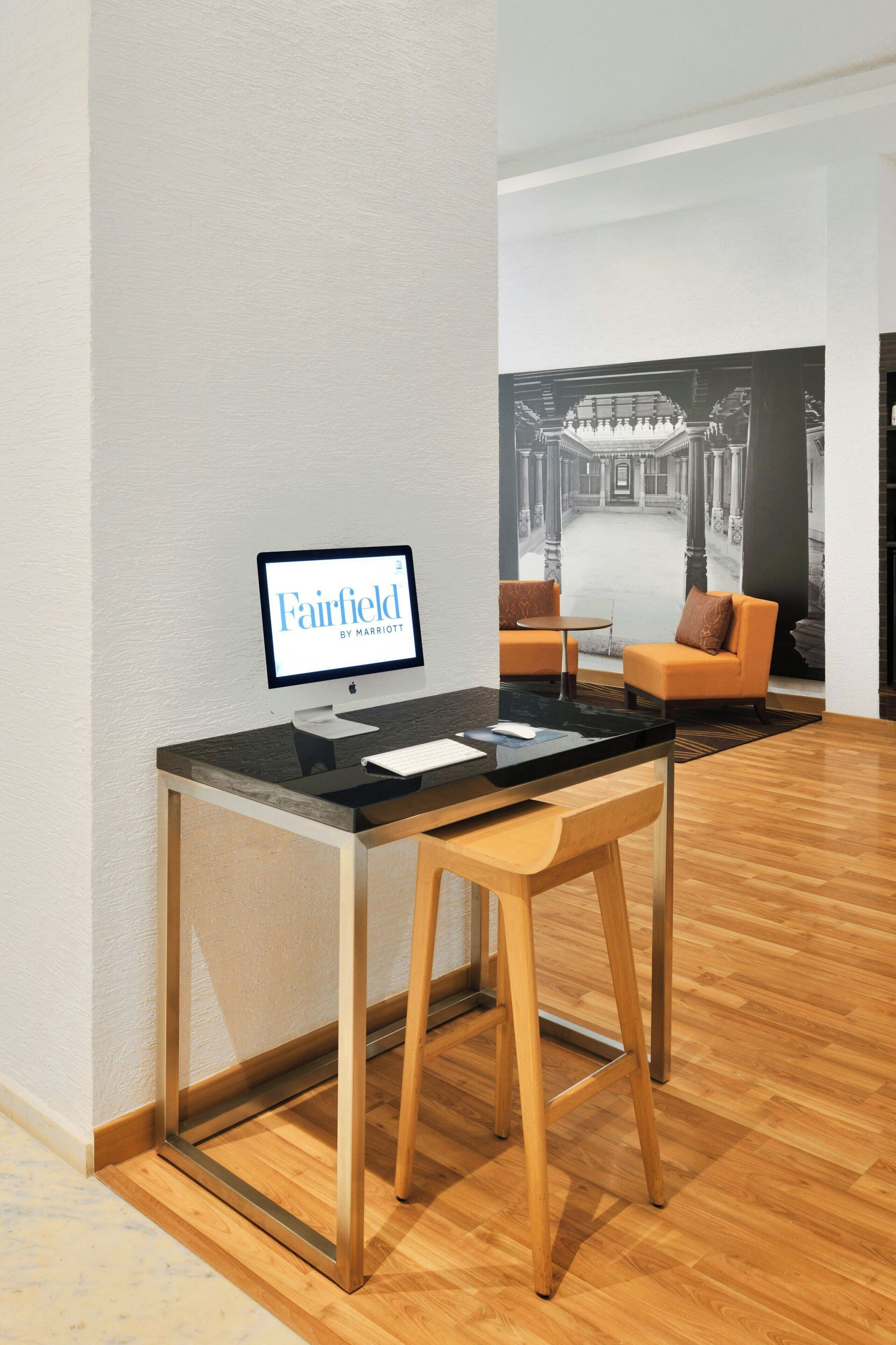 A hotel reception desk with a computer monitor displaying "Fairfield by Marriott," a wooden chair, and a sofa in the background.