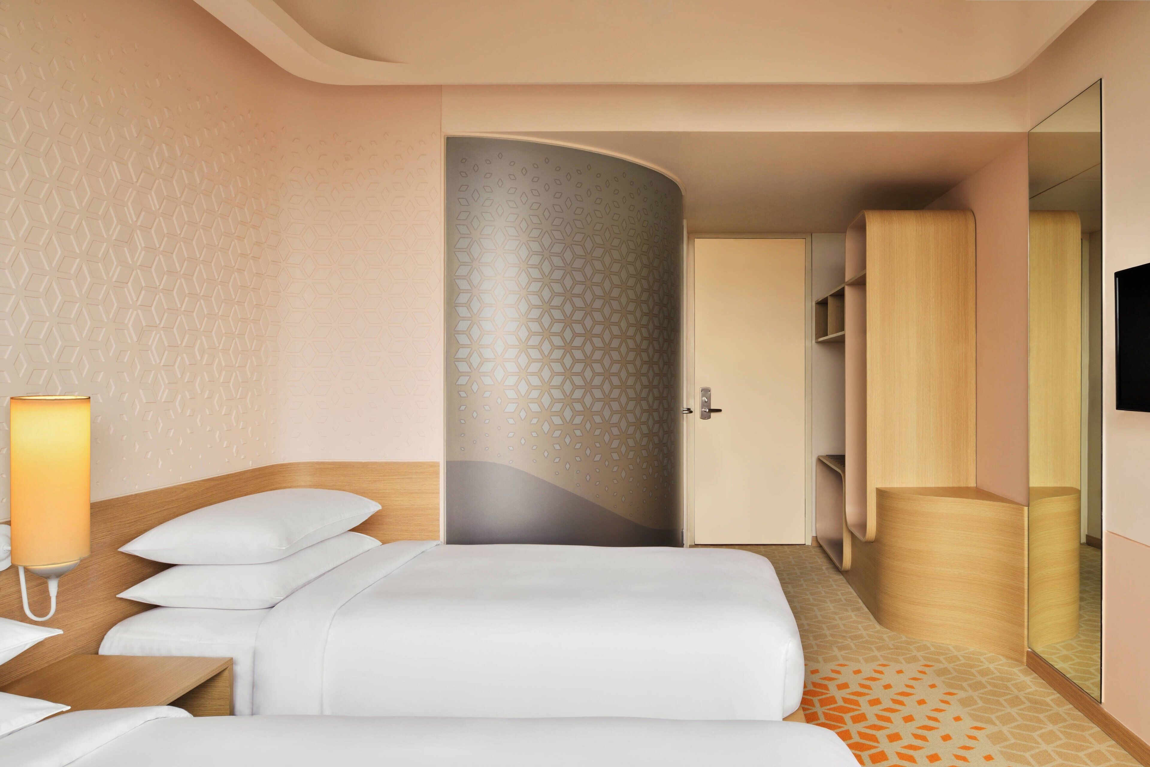 A hotel room with a bed, bedside table, lamp, wardrobe, and a mirror.