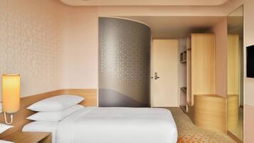 A hotel room with a bed, bedside table, lamp, wardrobe, and a mirror.